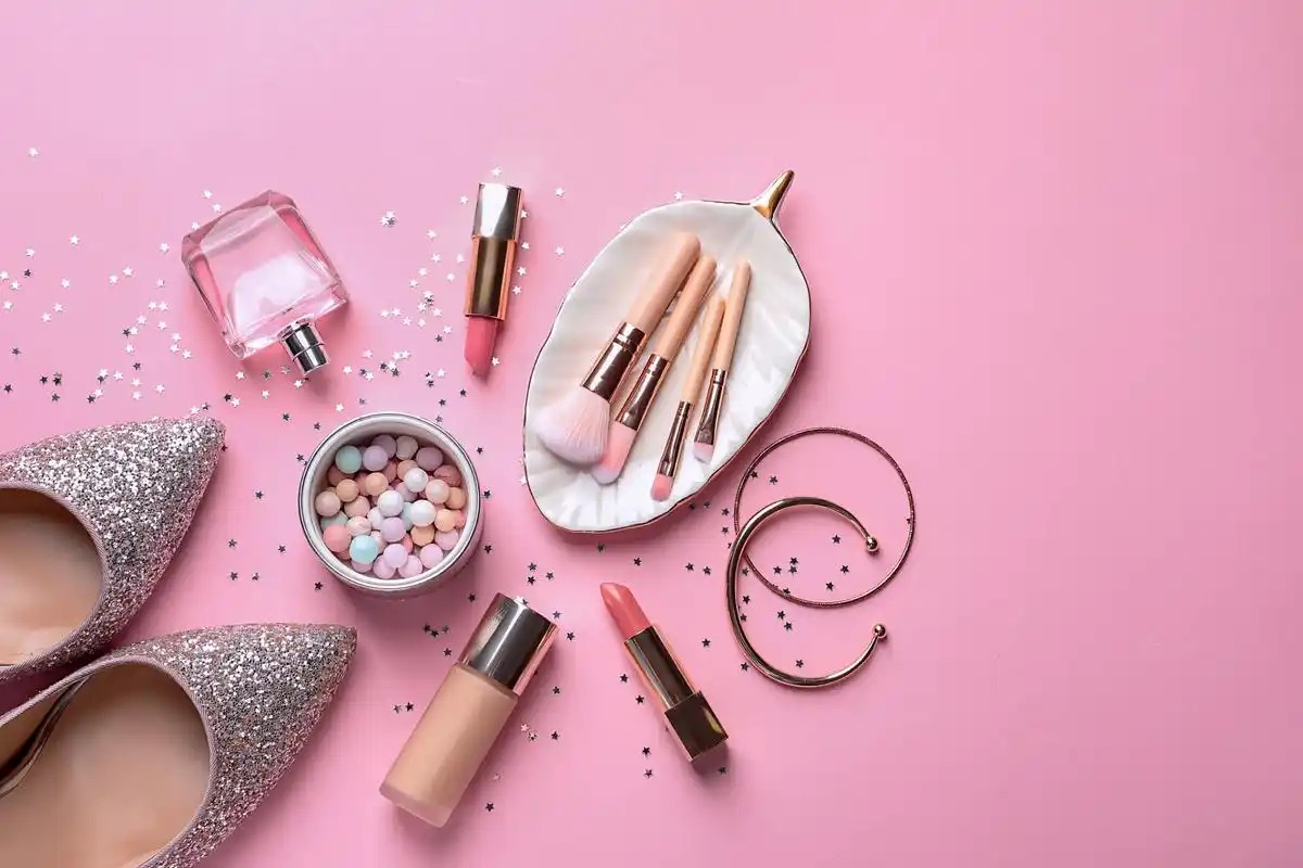 Flat-lay makeup dan sepatu berlatar merah muda untuk kampanye promo