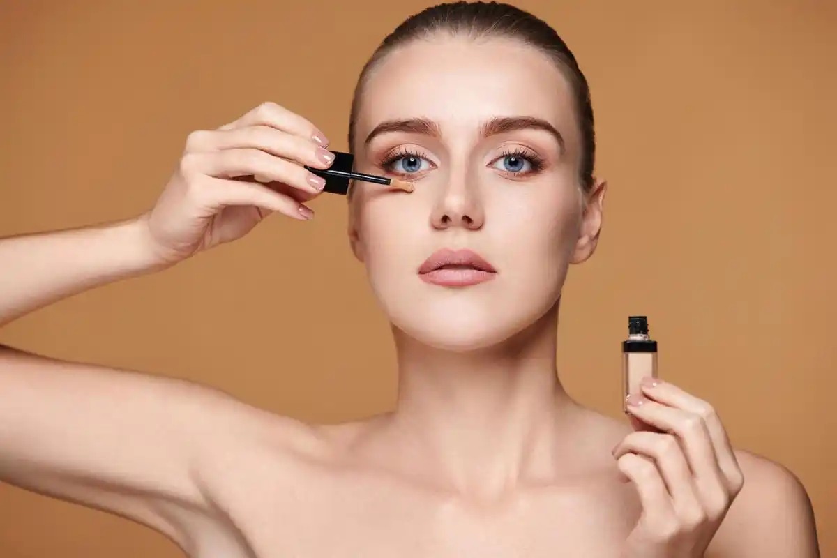 Model mengaplikasikan concealer dengan kuas di latar hangat