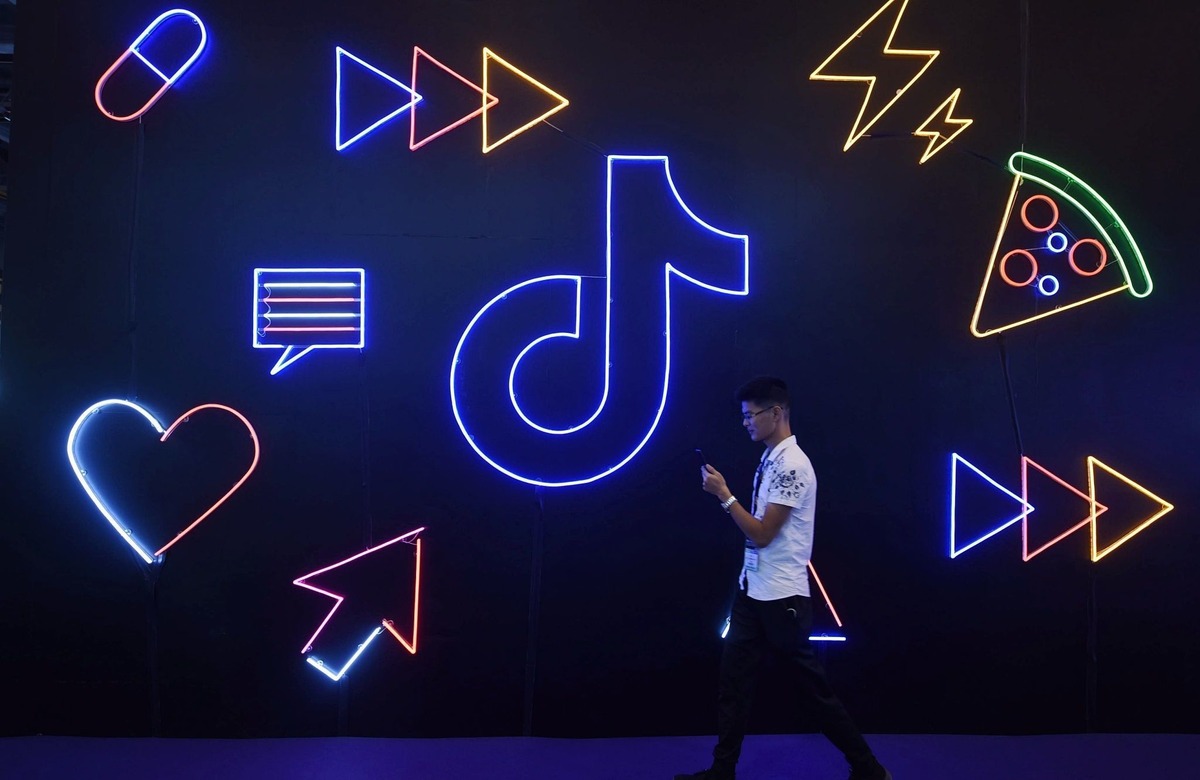 Seseorang berjalan melewati dinding ikon neon TikTok biru dan merah muda